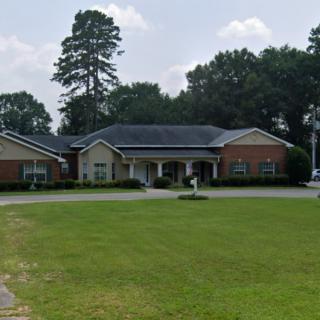 A large residential-style building with a well-kept lawn and surrounding trees.