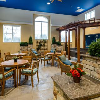 A well-lit interior dining area featuring wooden tables and chairs, accented by greenery and decor elements.