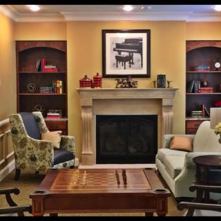 A cozy living room with a fireplace, surrounded by bookshelves and comfortable seating.