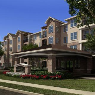 A modern residential apartment building with well-maintained landscaping under a clear blue sky.