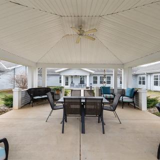 A cozy outdoor gazebo with a dining table, chairs, and comfortable seating set under a ceiling fan.