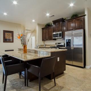 A modern kitchen with a dining area, featuring stainless steel appliances and a stylish countertop adorned with a vase of flowers.