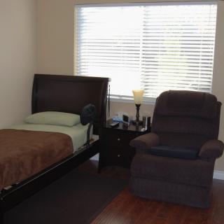 A simple bedroom with a single bed, recliner, and a window with blinds.