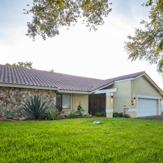 A suburban house with a spacious lawn and a garage, surrounded by trees.