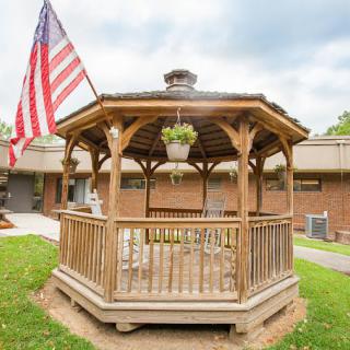 A wooden gazebo stands in a garden area, adorned with an American flag.