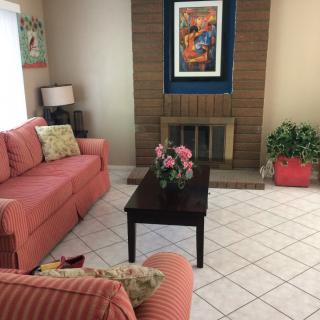 A cozy living room with a pink sofa, armchair, coffee table, and decorative elements like a fireplace and artwork.