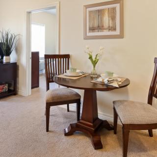 A cozy dining area featuring a small round table set for two with elegant chairs, adorned with a vase of flowers and artwork on the wall.