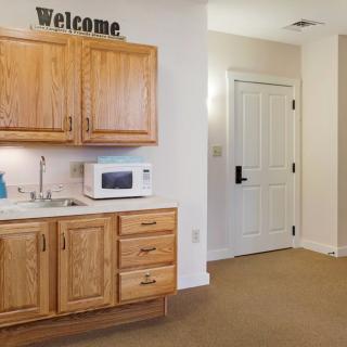 A small kitchenette with wooden cabinets and a microwave, featuring a welcome sign above.