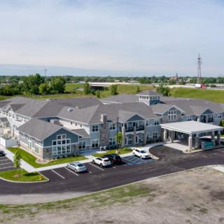 Aerial view of a large, modern building with a surrounding parking lot and green landscape.