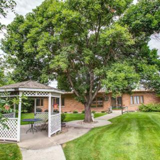 A serene garden with a gazebo, lush lawn, and mature trees surrounding a brick house.