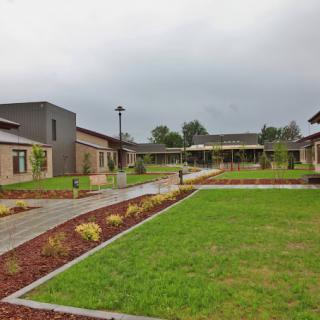 A courtyard with a walkway surrounded by modern buildings and green lawns under an overcast sky.