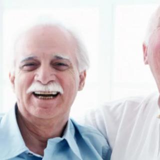 Two elderly men smiling together indoors.