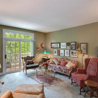A cozy living room with comfortable furniture, decorated with artwork and large windows overlooking greenery.