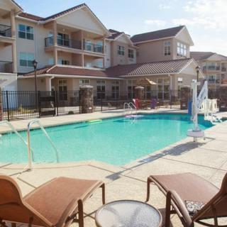 An outdoor swimming pool area in an apartment complex with sun loungers and a residential building in the background.
