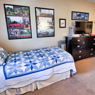 A cozy bedroom with a single bed featuring a blue quilt, a dresser with a TV on top, and wall posters.