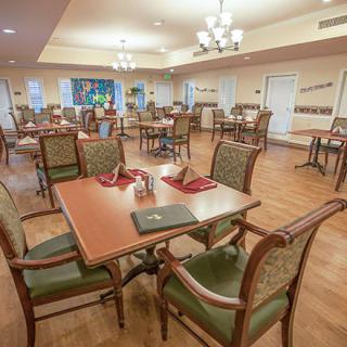 An empty dining room with neatly arranged tables and chairs, illuminated by chandelier lighting.