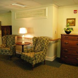 A cozy sitting area with two patterned chairs, a small table with a lamp, and a dresser topped with a plant.