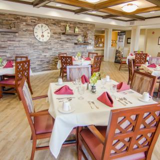 A well-decorated dining room with neatly arranged tables and chairs, featuring a stone wall and a large clock.