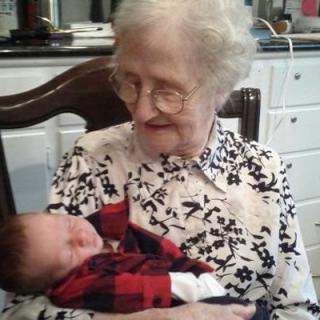 An elderly woman joyfully holds a sleeping baby indoors.