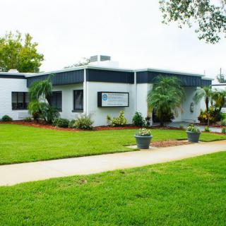 A small building surrounded by a well-maintained lawn and landscaping, featuring a clear pathway and several trees.