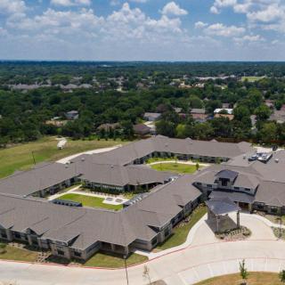 Aerial view of a large building complex surrounded by greenery and under a partly cloudy sky.