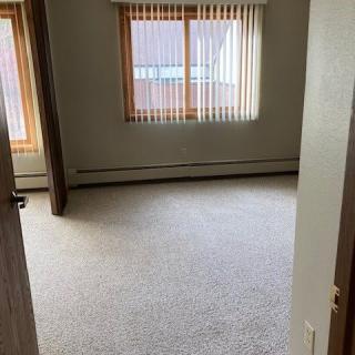 An empty room with carpet flooring and large windows letting in natural light.