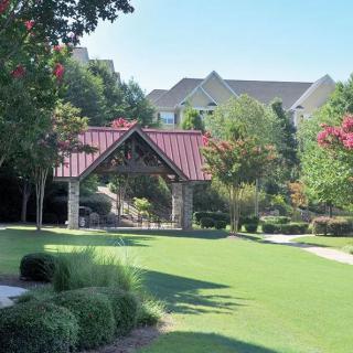 A serene park with a gazebo, surrounded by trees and a lush green lawn in a residential area.