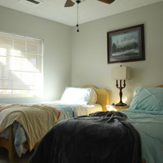 A cozy and inviting bedroom featuring two beds, a lamp, and a serene painting on the wall.