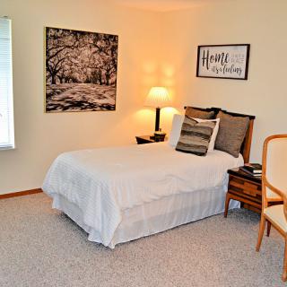 A cozy bedroom with a neatly made bed, decorative pillows, warm lighting, and wall art.