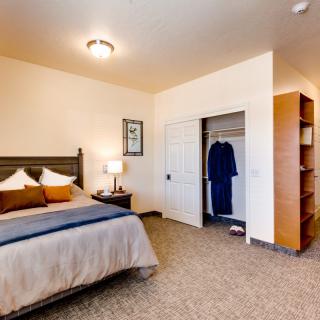 A cozy bedroom with a neatly made bed, open closet, and bedside table with a lamp.