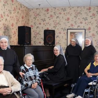 A group of nuns and elderly individuals gathered around a piano in a nursing home.