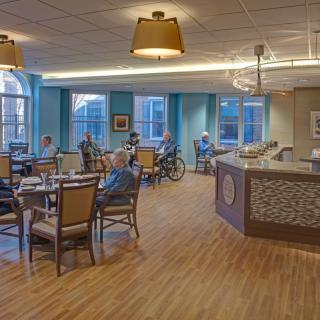 A cozy dining area in a senior living facility with tables, chairs, and people enjoying their meals.