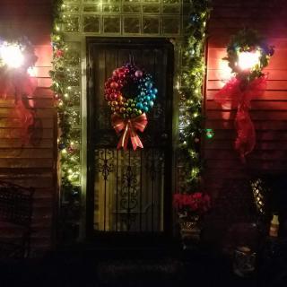 A festive front door decorated with a colorful Christmas wreath and glowing lights.