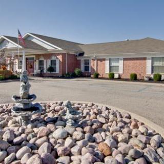 A single-story brick building with a circular driveway featuring a fountain surrounded by rocks.