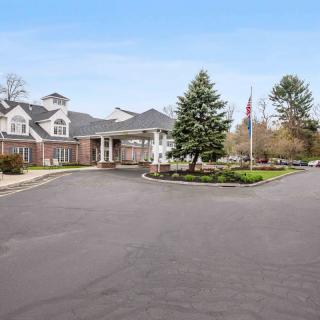 A large residential building surrounded by trees with a driveway leading to the entrance.