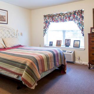 A cozy bedroom featuring a neatly made bed with a striped quilt, framed photographs on the window sill, and classic wooden furniture.