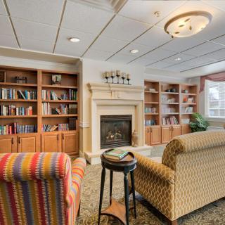 A cozy library reading room with comfortable armchairs and a fireplace surrounded by bookshelves.