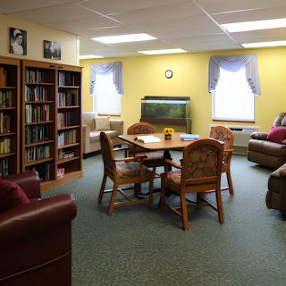 Cozy library room with bookshelves, a table, chairs, sofas, and a fish tank.