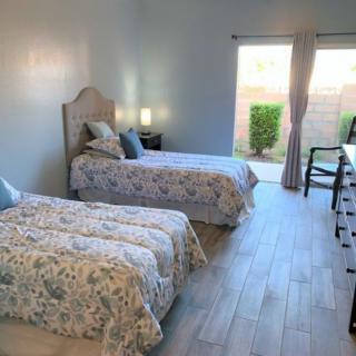 A bright bedroom with twin beds, featuring floral bedding and a view of the outdoors.