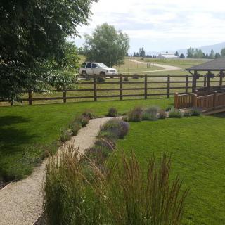 A well-maintained garden with a grassy lawn, pathway, and wooden fence in a rural setting.
