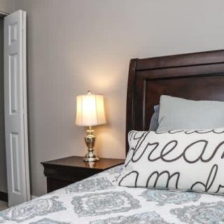 A cozy bedroom featuring a bed with decorative pillows, a nightstand, and a lamp.