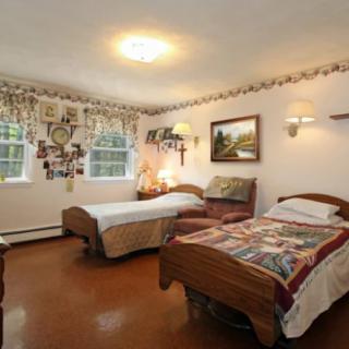 A cozy bedroom featuring two twin beds with decorative quilts, adorned with traditional decor and wall art, illuminated by natural light through the windows.