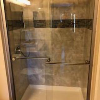 A modern shower with a glass door and tiled interior.