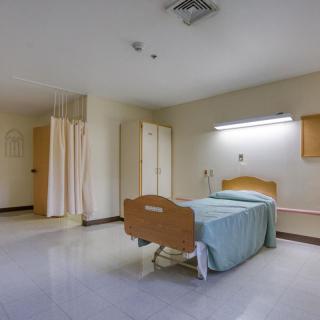 An empty hospital room with a single bed and lighting on the wall.