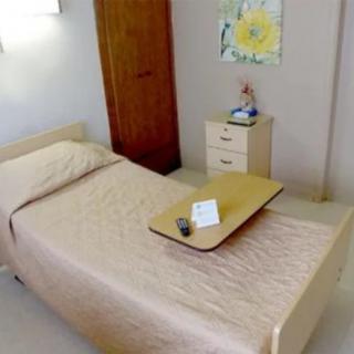 A tidy, minimalist bedroom with a single bed, small cabinet, and warm lighting.