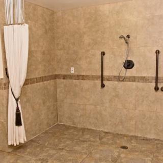 A spacious accessible bathroom with grab bars and a walk-in, curtain-covered shower.