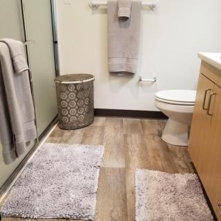 A modern bathroom featuring neatly arranged towels, rugs, and a laundry hamper.