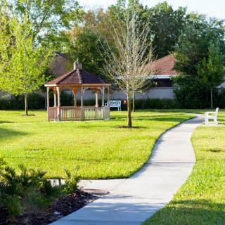 A serene park scene featuring a winding pathway leading to a wooden gazebo, surrounded by lush green grass and trees.