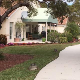 A quaint house with a green awning, surrounded by well-maintained landscaping and a curved pathway.