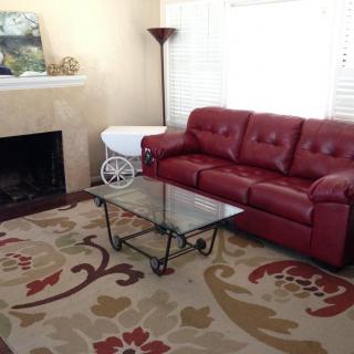 A cozy living room featuring a red leather sofa, glass coffee table, patterned rug, and fireplace.